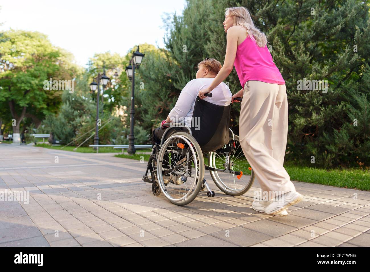 Young female caregiver pushing wheelchair with female person with