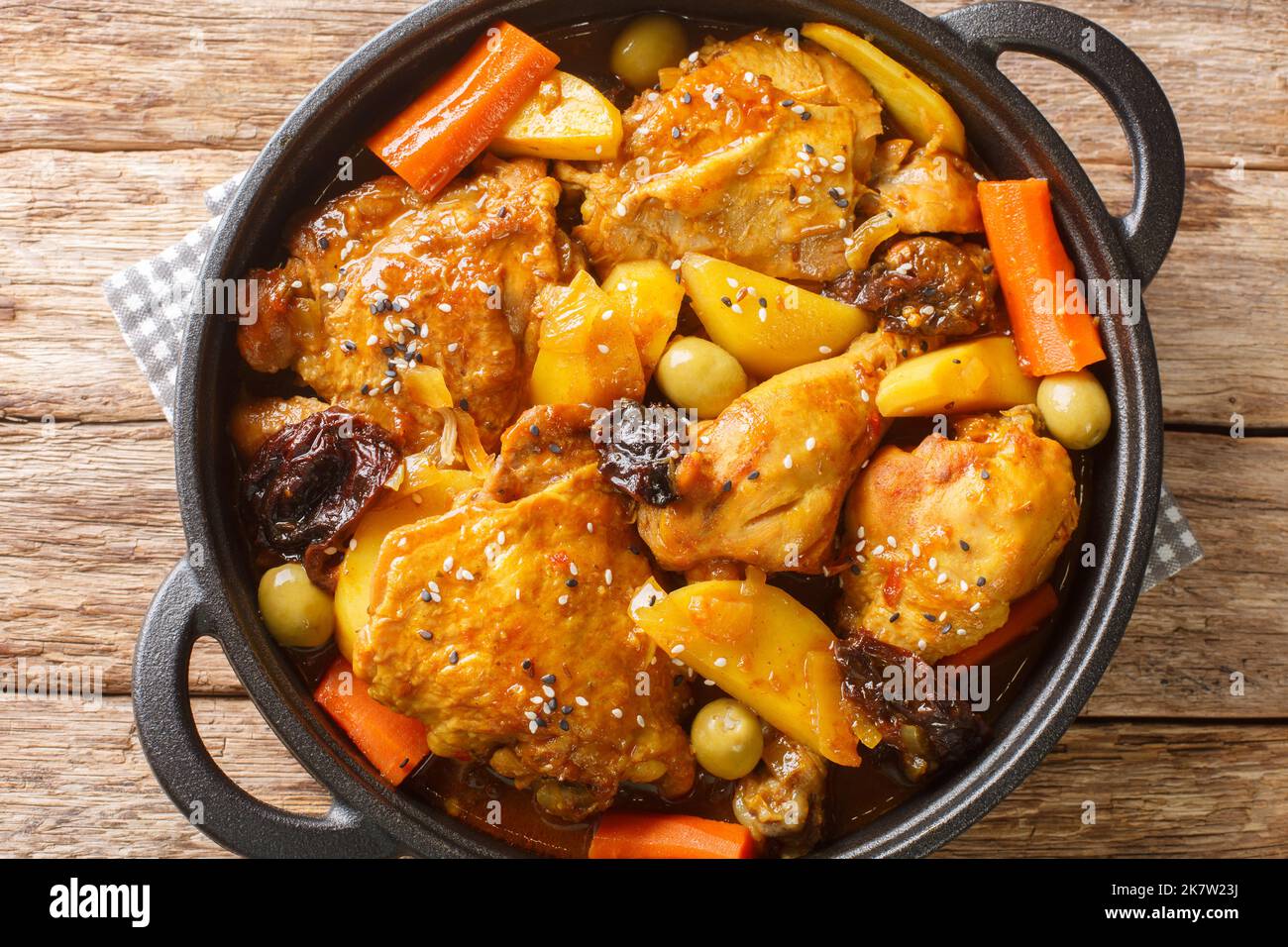 Salvadoran chicken stew with chicha, prunes, carrots, potatoes, olives and onions close-up in a frying pan on a wooden table. Horizontal top view from Stock Photo