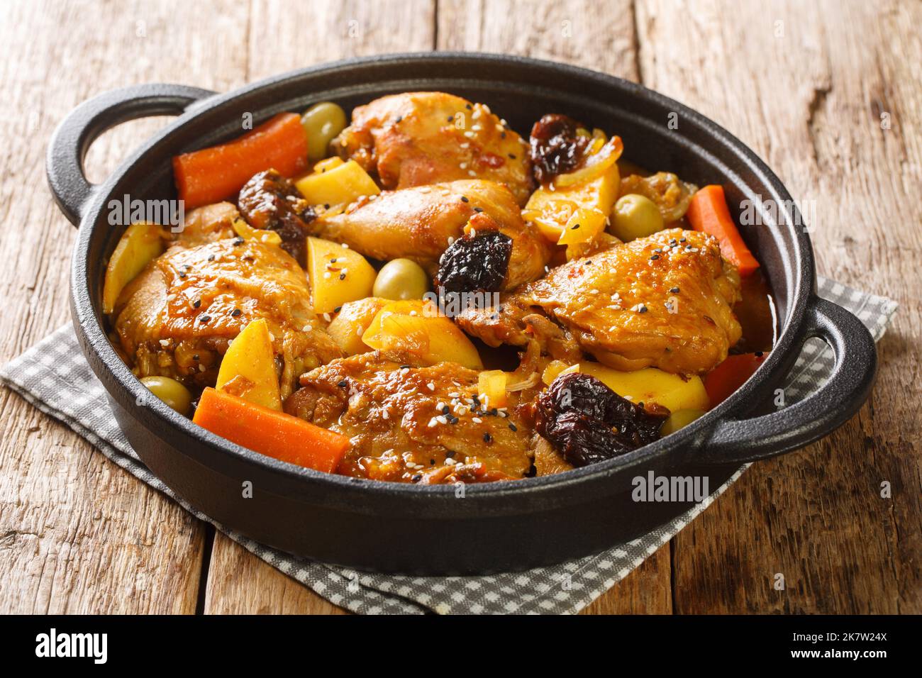 Salvadoran chicken stew with chicha, prunes, carrots, potatoes, olives and onions close-up in a frying pan on a wooden table. Horizontal Stock Photo