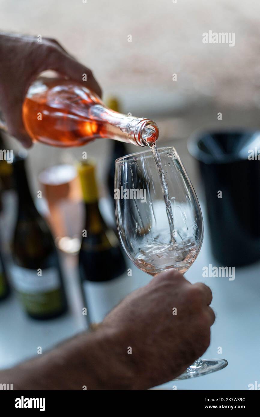 Close up of a man pouring a bottle of rose wine into a wine glass Stock Photo