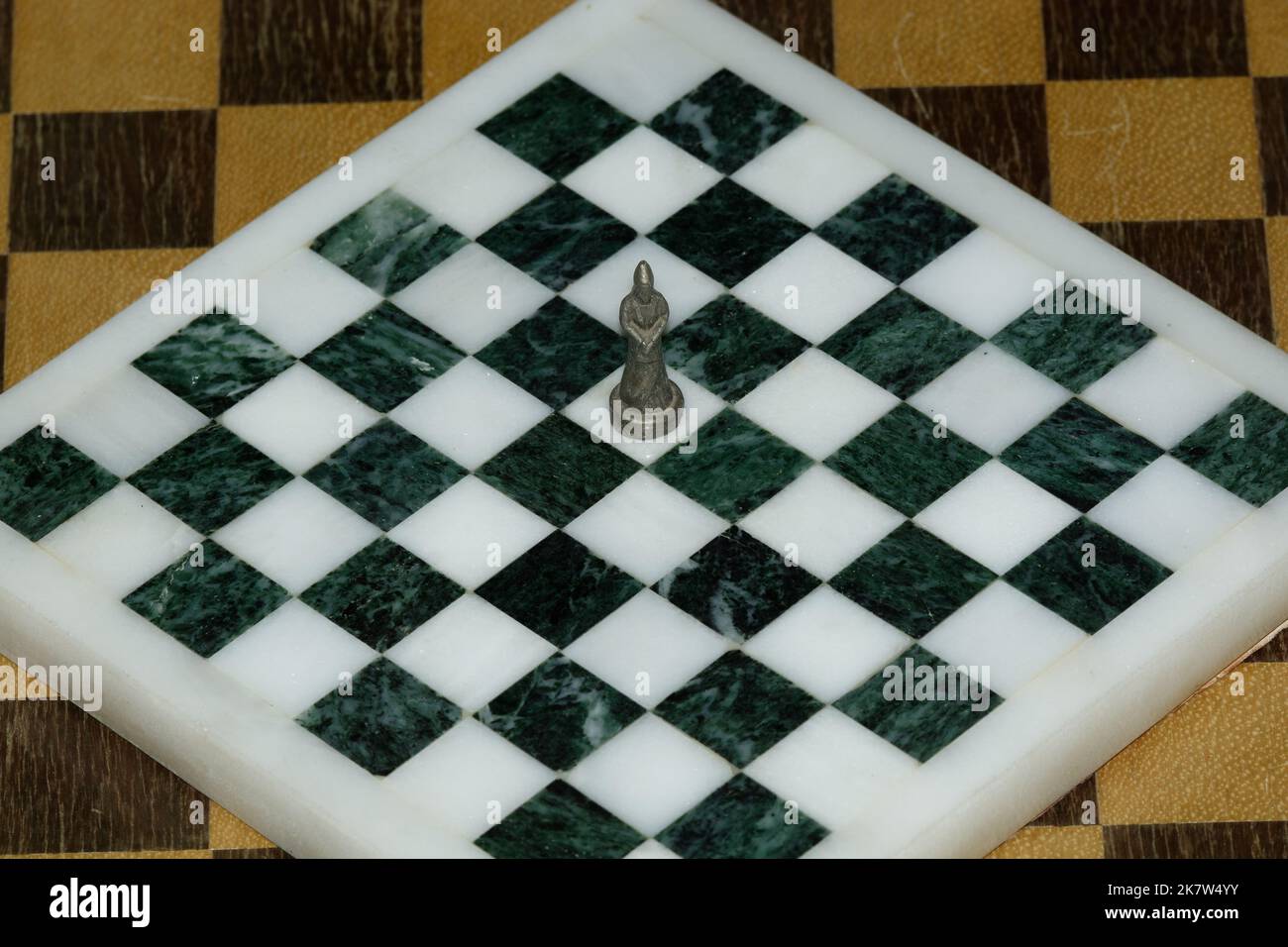 Lone Queen standing the centre of a black and white marble chess board. No other pieces are present. Wonderful sense of solitude or abandonment. Stock Photo