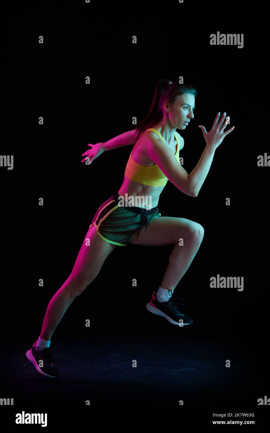 Professional female athlete running isolated on dark background in neon