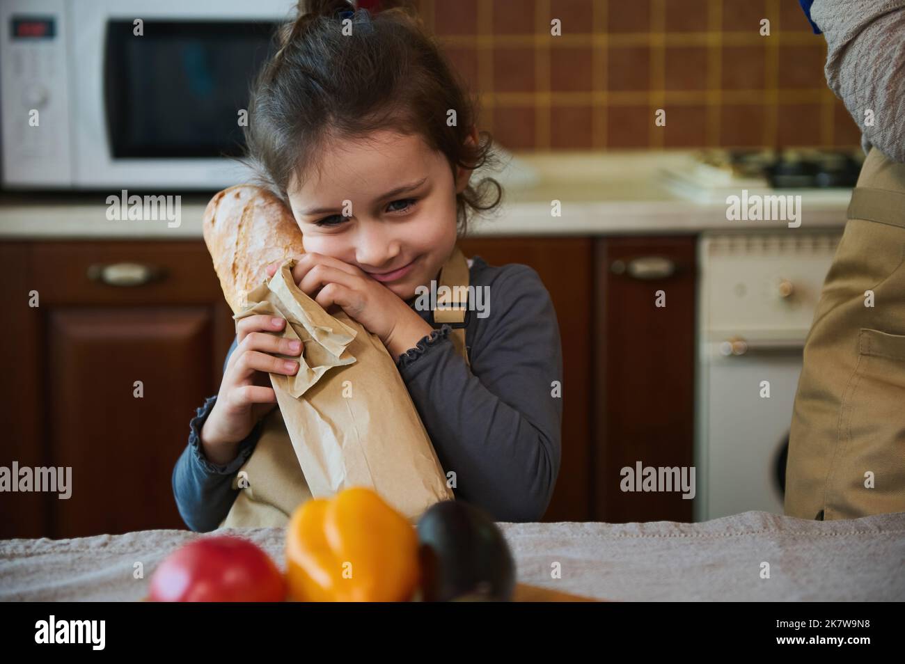 Close-up portrait of a cute little girl hugging a loaf of sourdough bread from family bakery while unpacking grocery bag Stock Photo