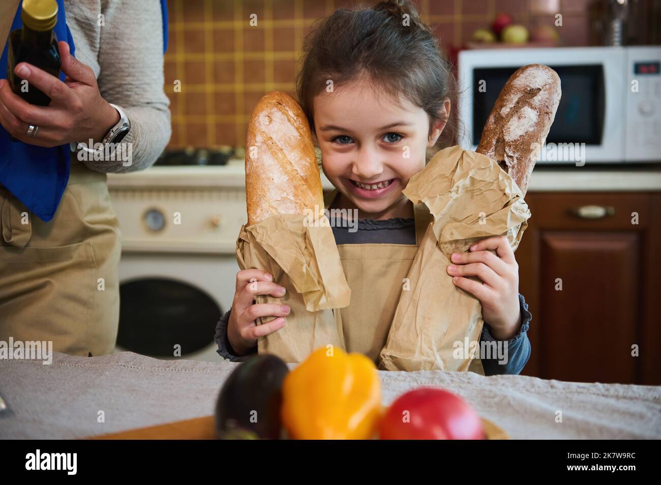 Charming kid, little girl with two loaves of sourdough wheat whole grain bread, smiling a toothy smile looking at camera Stock Photo