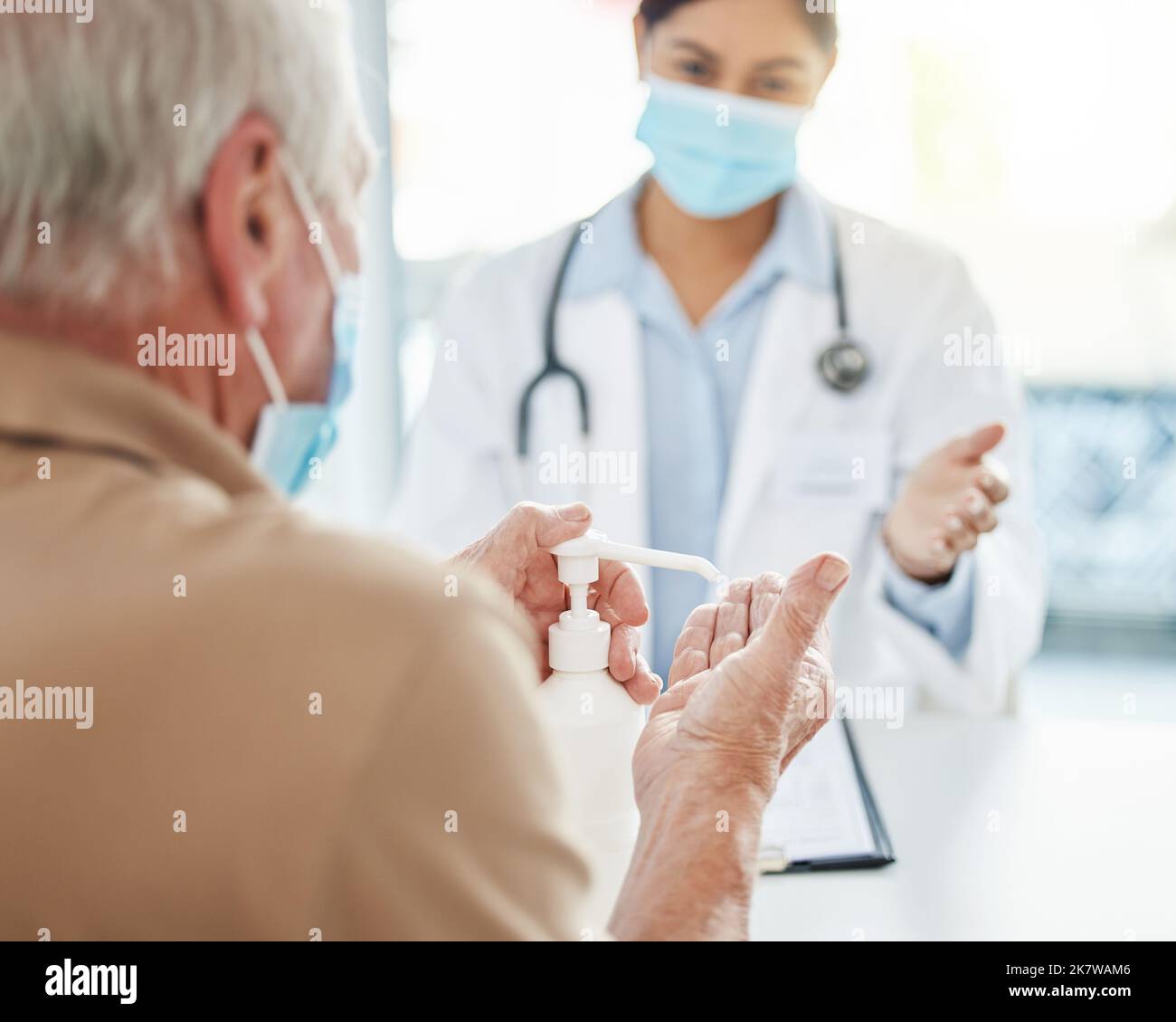 Lets get those hands germ-free. an unrecognizable man sitting with his doctor and using hand sanitiser during his consult in the clinic. Stock Photo