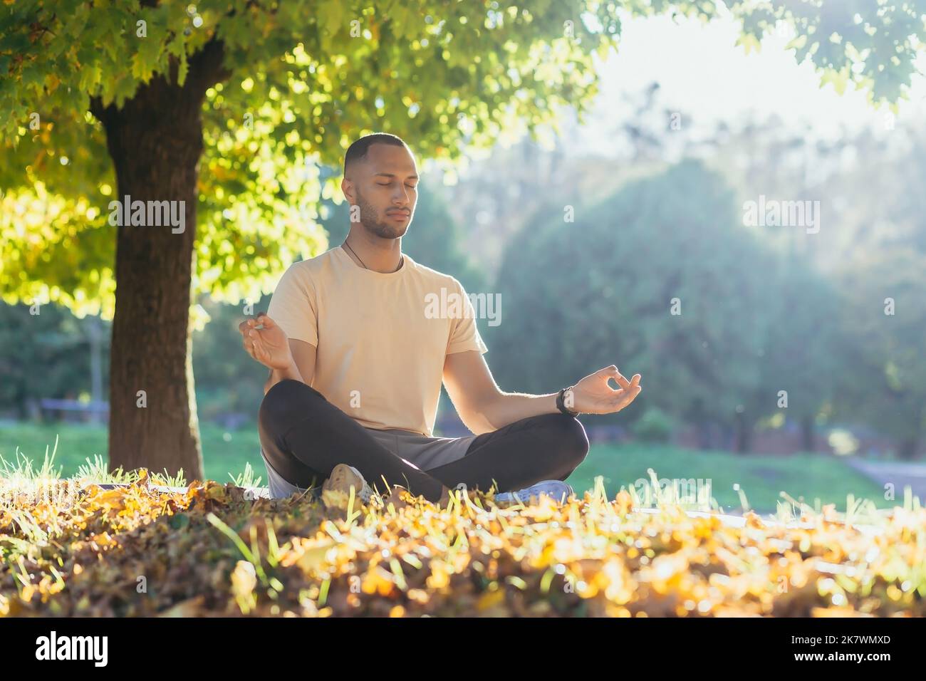 A young man meditates in the park at sunset, an athlete in the lotus ...