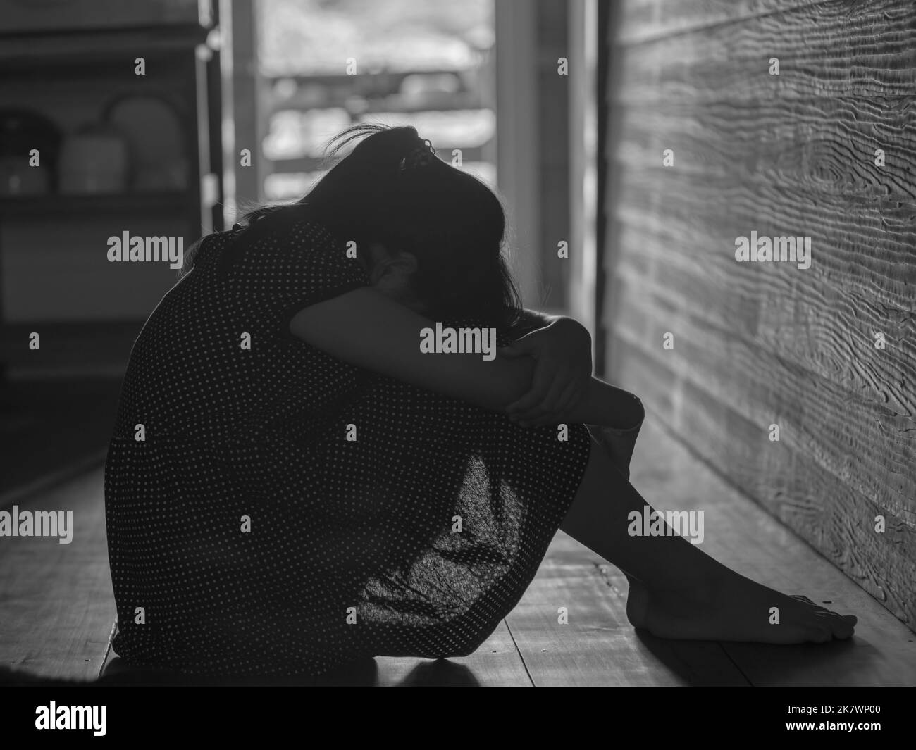 Sad lonely little girl crying while sitting on the floor in dark room with an attitude of sadness.Concept of depression or domestic violence child.Bla Stock Photo