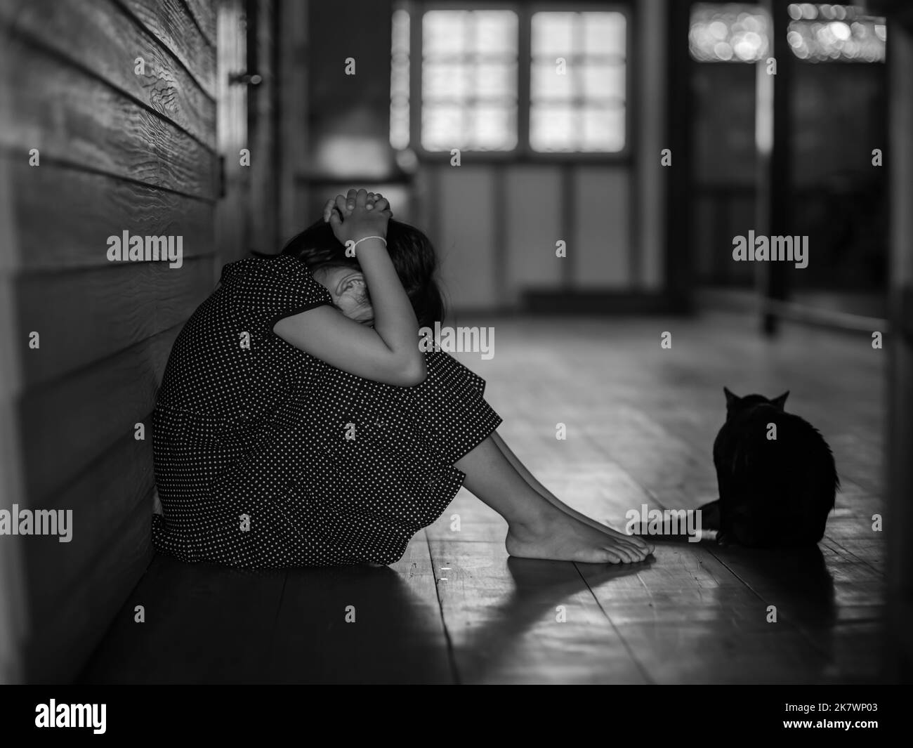 Sad lonely little girl crying while sitting on the floor in dark room with an attitude of sadness and black cat sit with her.Concept of depression or Stock Photo