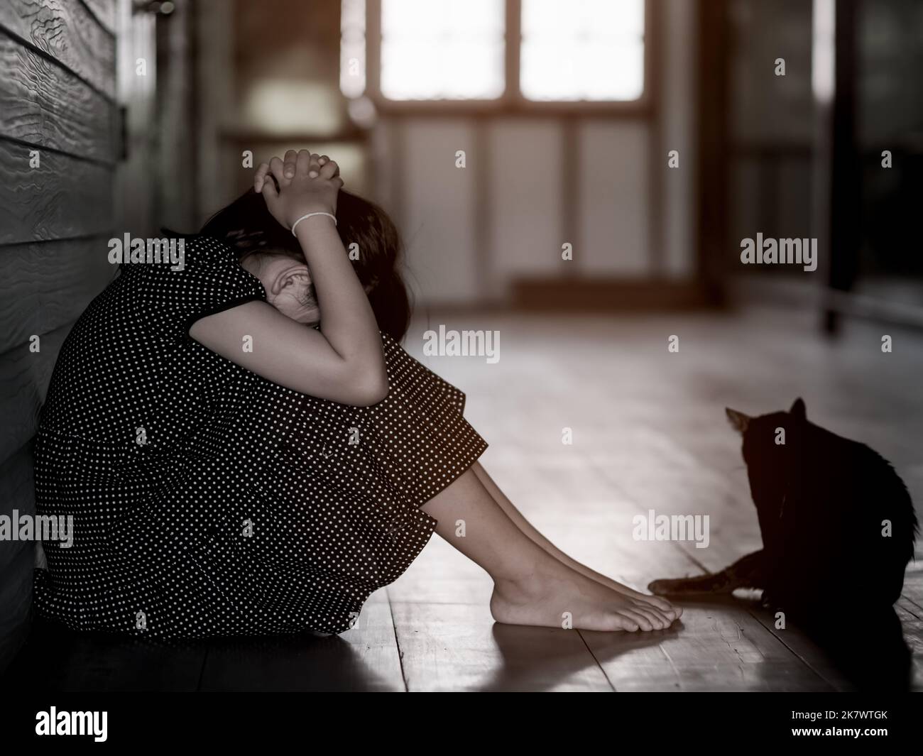 Sad lonely little girl crying while sitting on the floor in dark room with an attitude of sadness.Concept of depression or domestic violence child Stock Photo