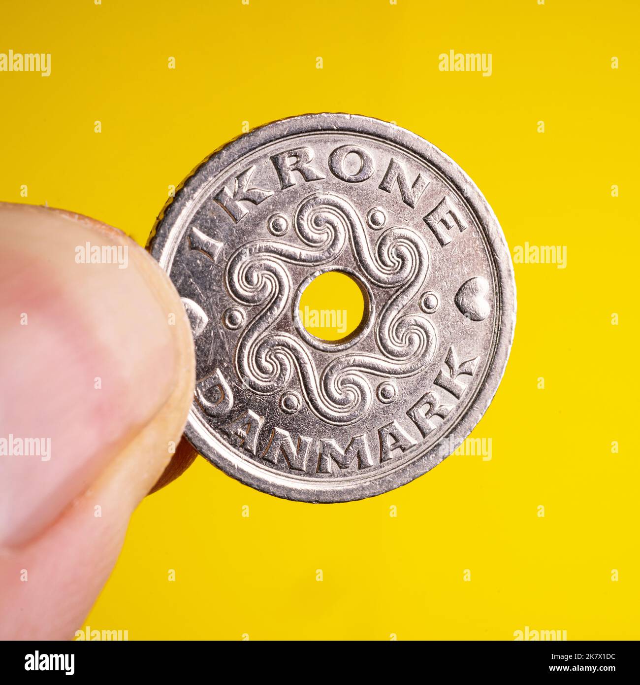 a Danish krone coin between the fingers of the hand Stock Photo