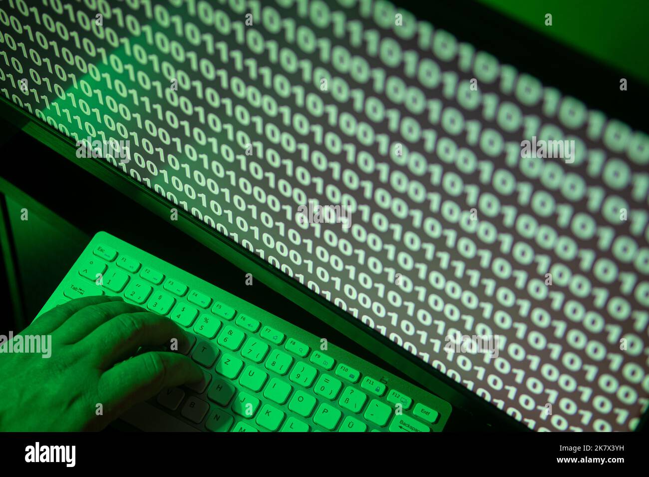 hand on keybord with binary code on a screen, green illuminated Stock Photo
