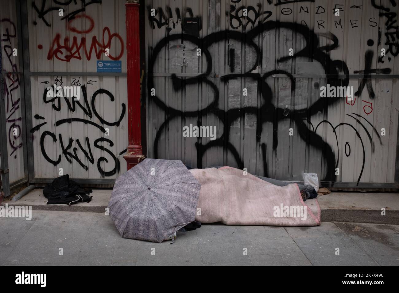 Homeless person asleep in front of graffiti wall, in Porto, Portugal, 16 October, 2022. Stock Photo