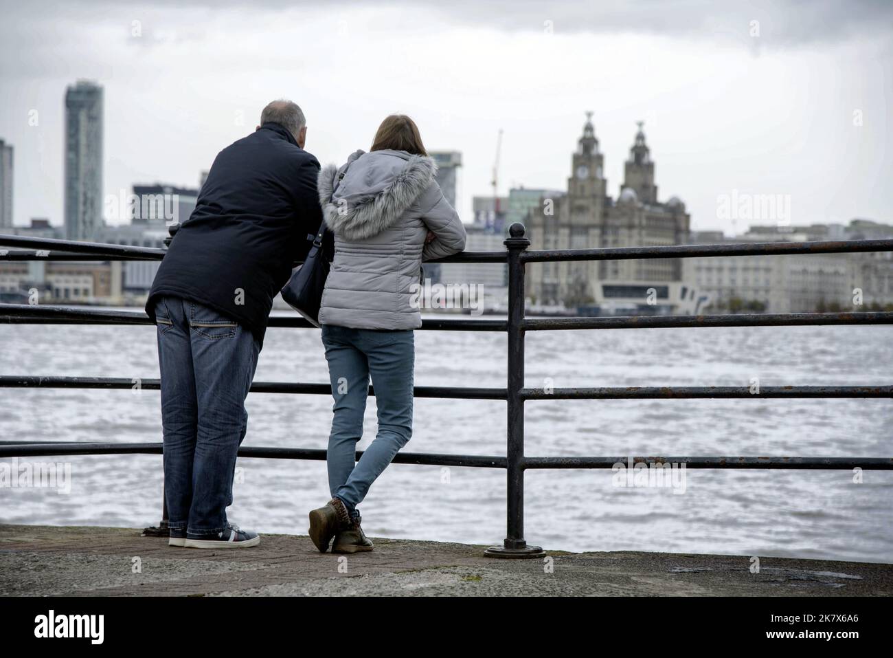 A couple gaze across the river Mersey at the Royal Liver building on the waterfront from Seacombe. Stock Photo