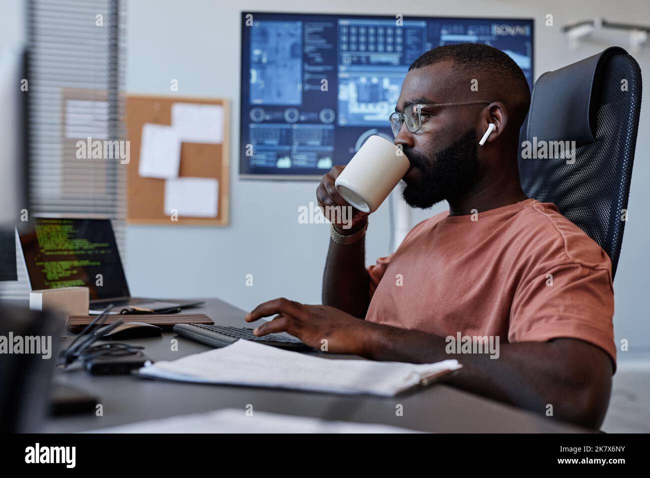 Side view portrait of black man drinking coffee at workplace while working in IT software development Stock Photo