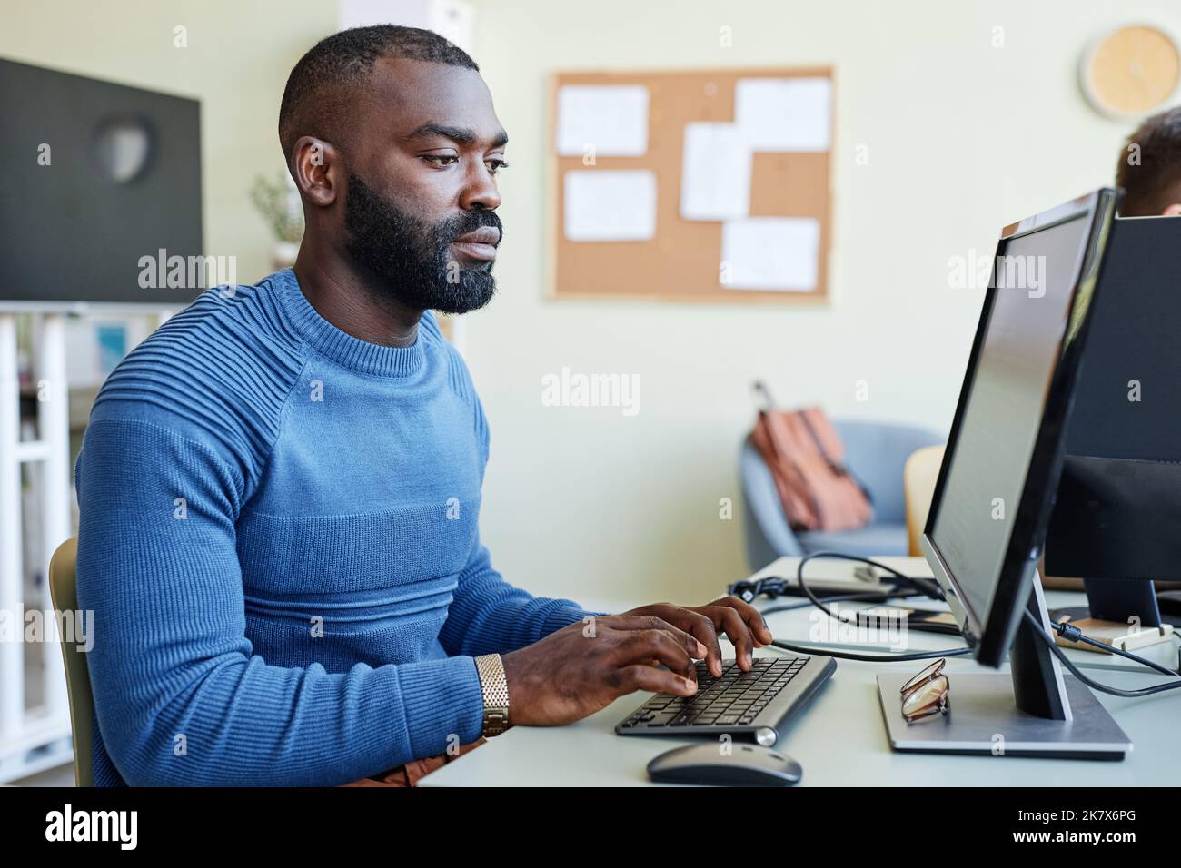 Side view portrait of bearded black man using laptop in office while programming software Stock Photo