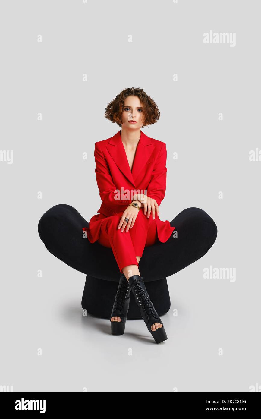 Young woman in red pantsuit sits in armchair and listens attentively Stock Photo