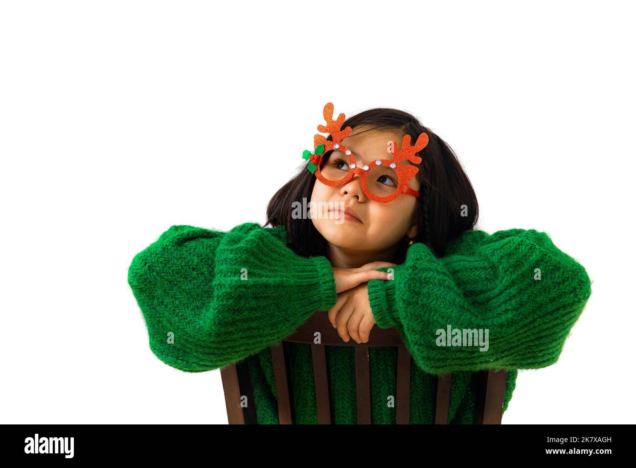 Cute asian child girl in green sweater and masquerade christmas glasses with deer horns. Portrait Beautiful Thai girl looking up to the side wearing a Stock Photo