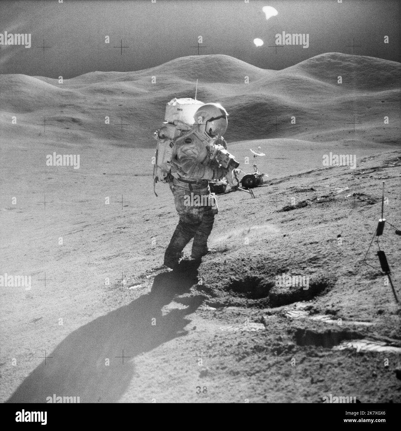 Astronaut David R. Scott, commander, standing on the slope of Hadley Delta, uses a 70mm camera during Apollo 15 extravehicular activity (EVA) on the lunar surface, July 31, 1971. He is 10.5 miles (or 17.5 kilometers) from the base of the Apennine Mountains seen in the background. Scott carries tongs in his left hand. The Lunar Roving Vehicle (LRV) is in the background. Stock Photo