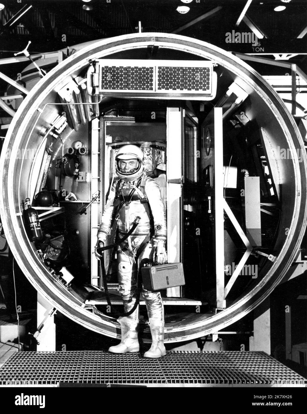 Astronaut John H. Glenn Jr., suited with hose to suit ventilation unit attached, during altitude chamber test. He is standing in the entrance to the test chamber with his helmet visor down. Stock Photo