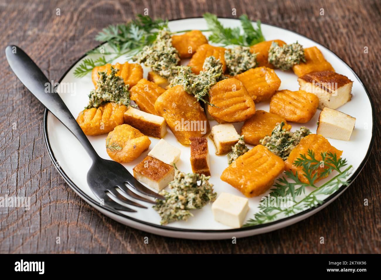 Plate with home made carrot gnocchi with a carrot-top pesto and smoked tofu. Stock Photo