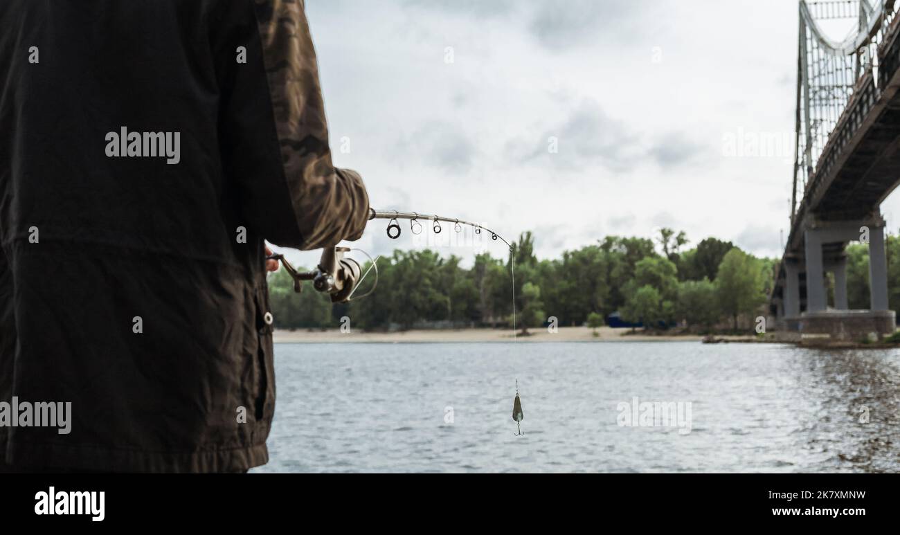Young man fishing on the river. Fisherman holding spinning rod with spoon bait Stock Photo