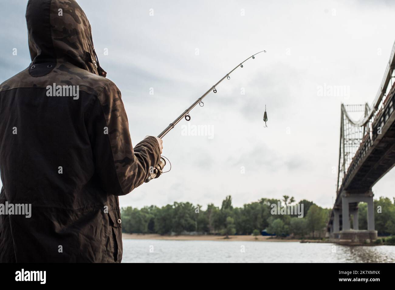 Young man fishing on the river. Fisherman holding spinning rod with spoon bait Stock Photo