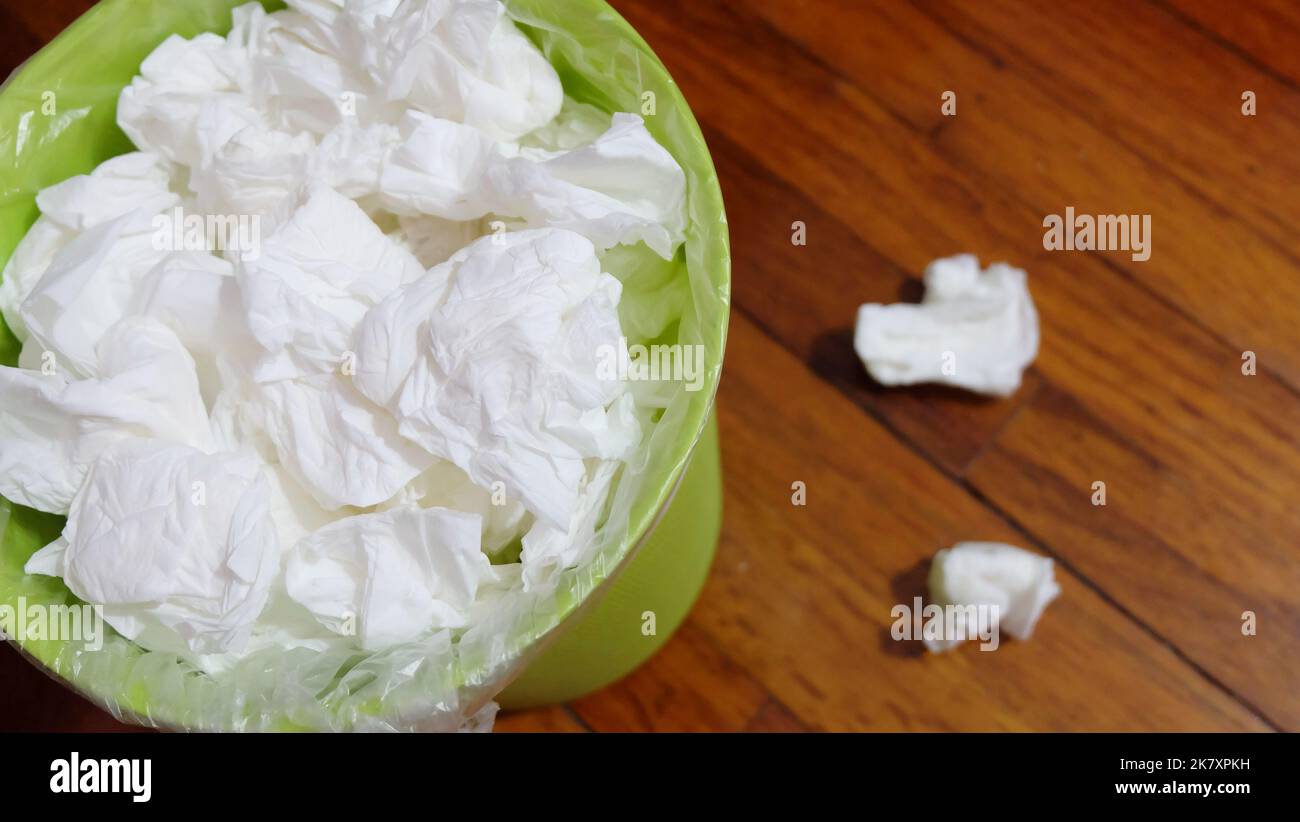 A small garbage bin full with used tissue paper, on a wooden floor. Stock Photo