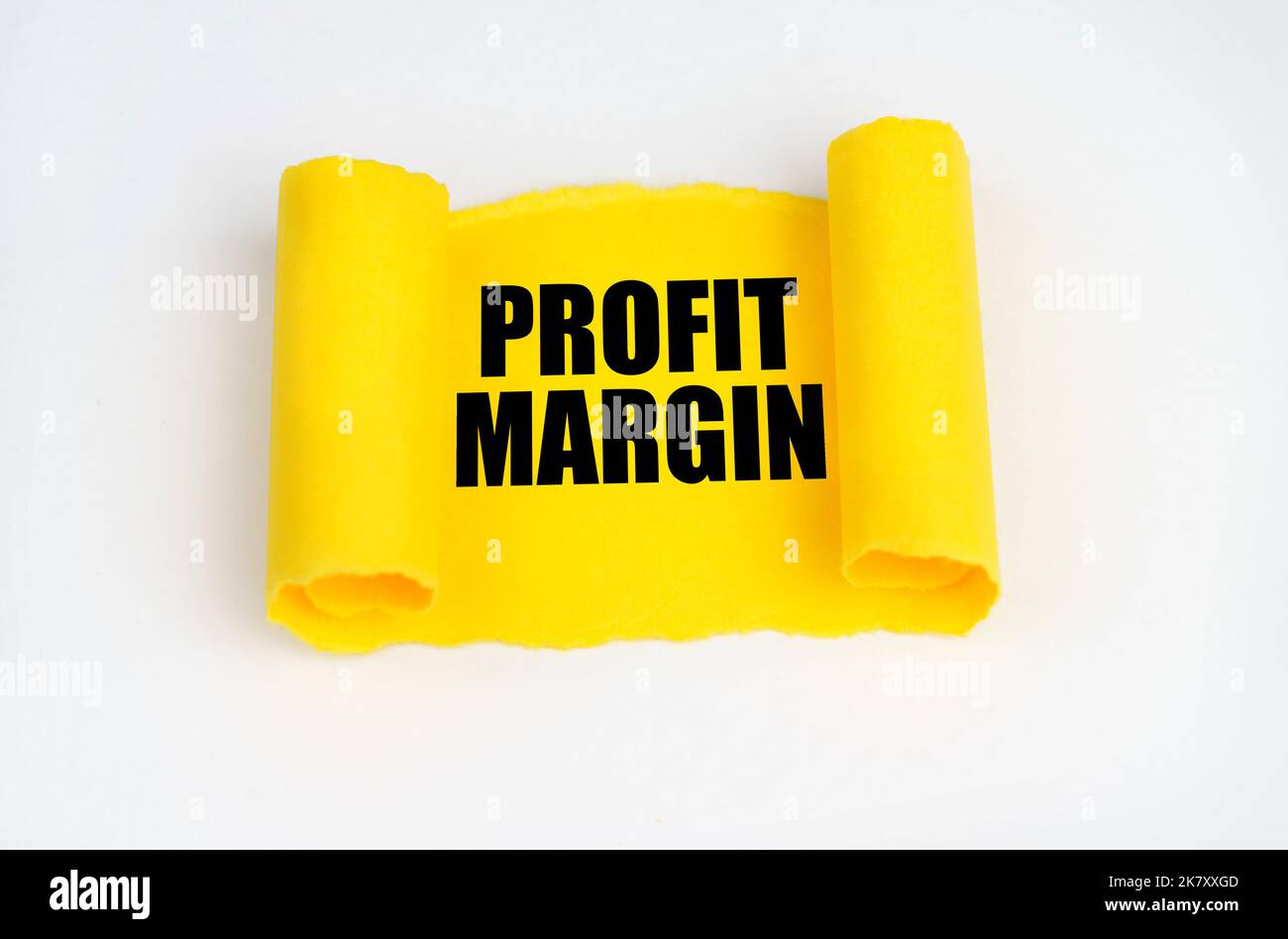 On a white surface, a yellow scroll of paper with the inscription PROFIT MARGIN. Business
