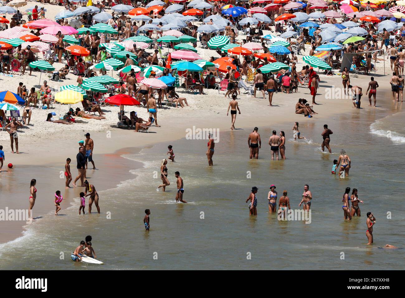 Leblon beach, Rio de Janeiro, Brazil. People sunbathing near shore with colorful umbrellas. Crowd enjoy summer day swimming at sea. Tropical travel Stock Photo
