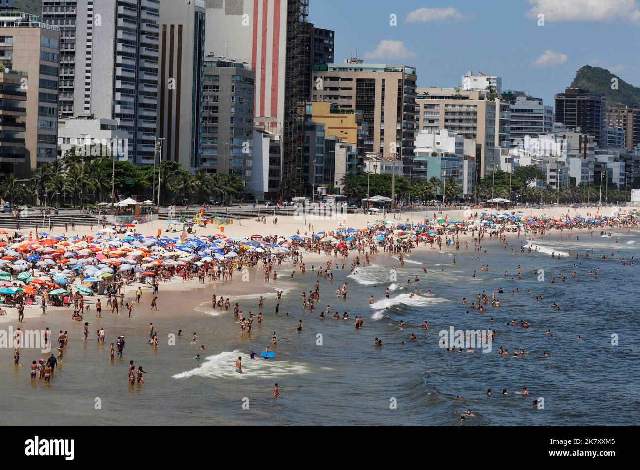 Leblon beach, Rio de Janeiro, Brazil. People sunbathing near shore with colorful umbrellas. Crowd enjoy summer day swimming at sea. Tropical travel Stock Photo