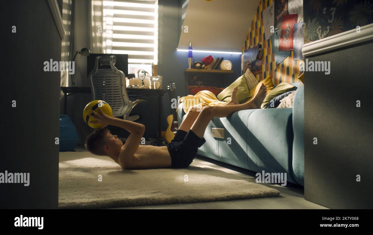 Young boy do abs crunches while holding football in his hands and