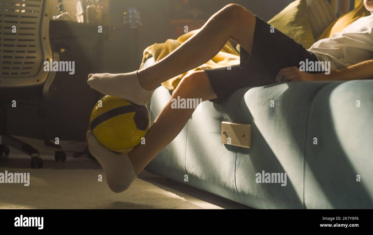 Young boy closeup feet movement kicks the football in his bedroom. Performs tricks with the ball. Soccerr, sports, hobbies, athletes cocept. Stock Photo