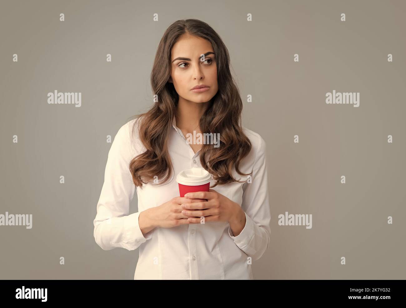 Portrait of nice cute girl holding cup of coffee. Young woman smiling with a coffee cup, isolated on gray background. Stock Photo