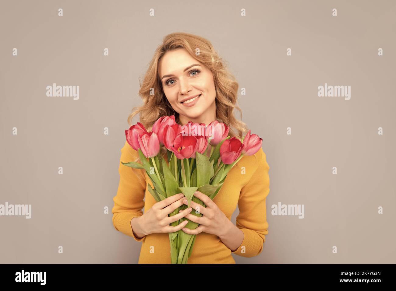 smiling lady hold flowers for spring holiday on grey background Stock Photo