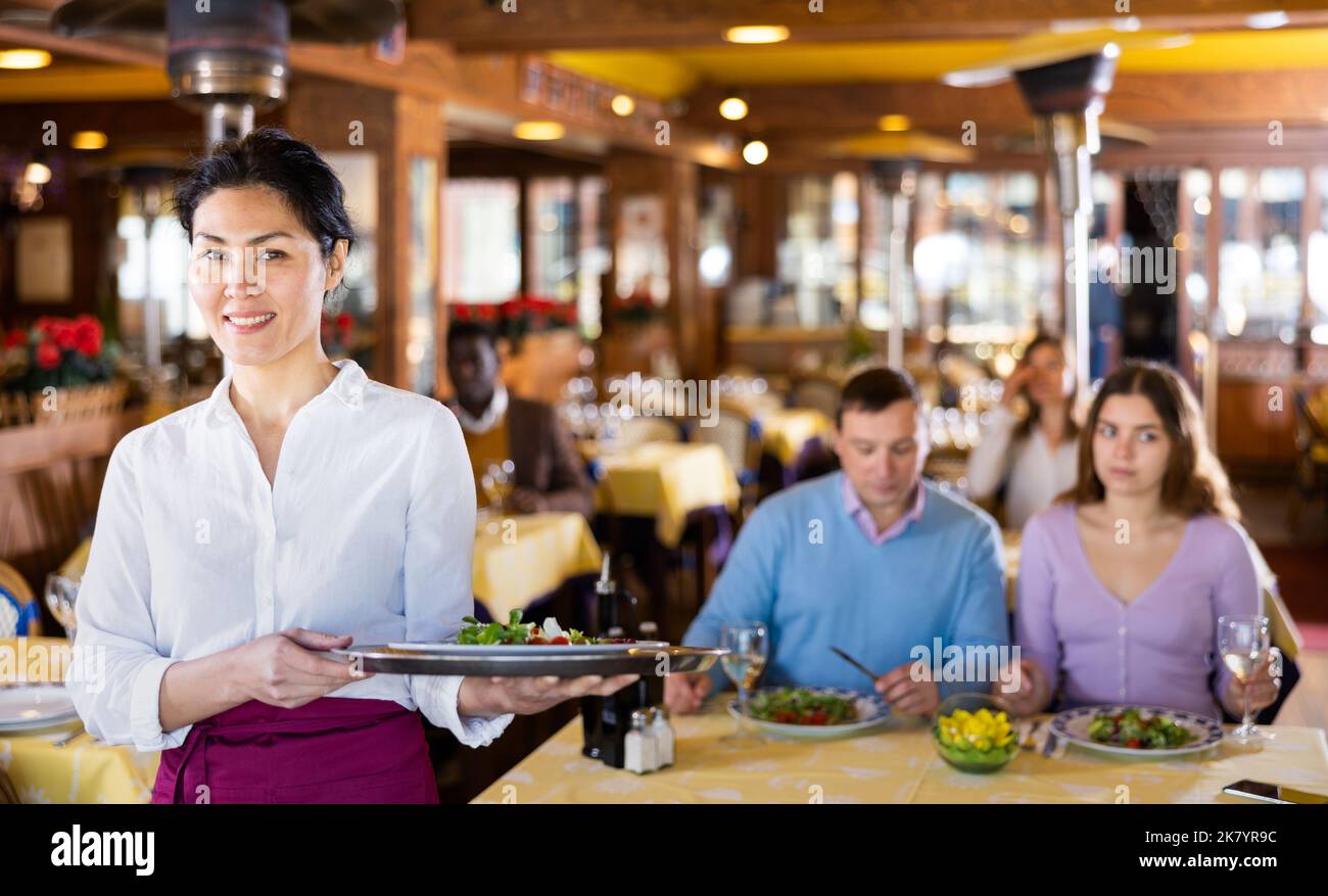 Polite smiling asian waitress inviting to cozy restaurant Stock Photo ...