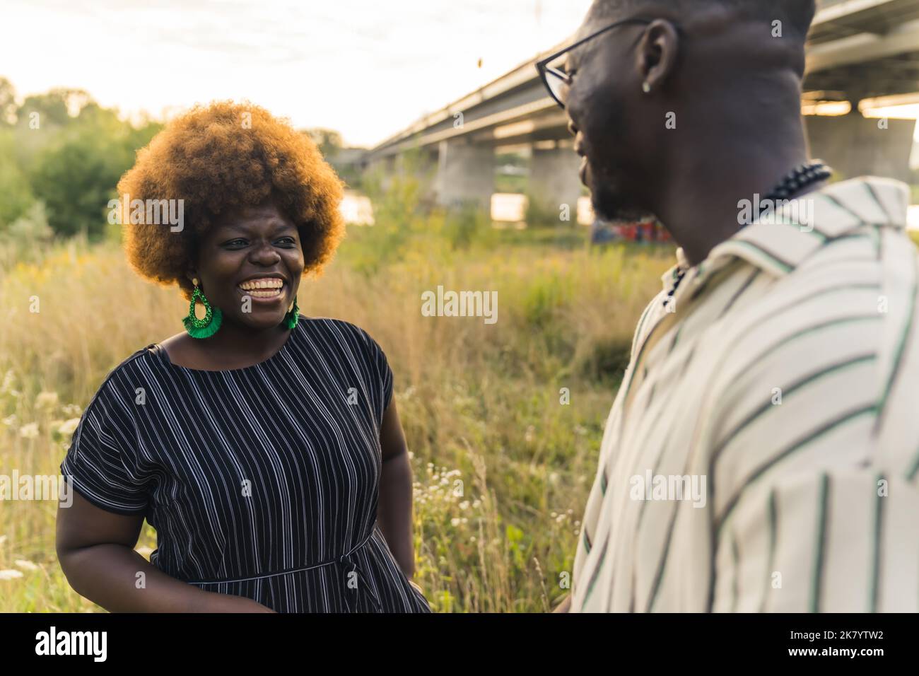 Lovely African-American couple standing by the river, in the middle of meadow, laughing and flirting with each other. Human relationships. Two Black people - a woman and a man - in stripped casual clothes talking. High quality photo Stock Photo