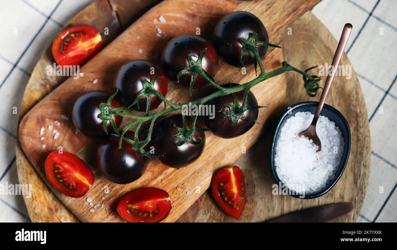 Black tomatoes on a branch on a wooden board with sea salt. Stock Photo