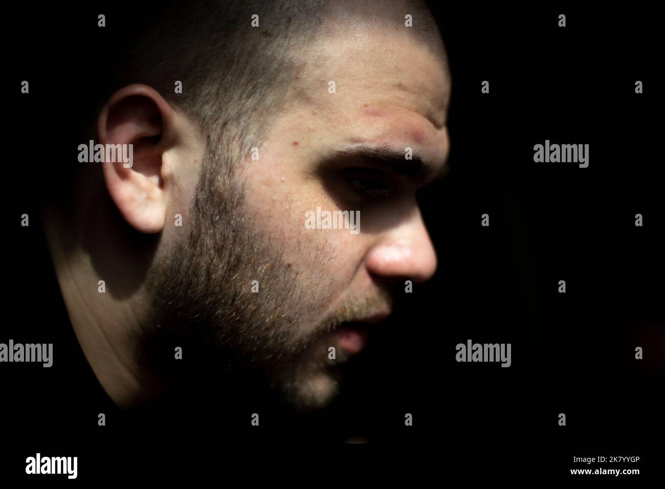 Guy face is on black background. Man in light. Young guy side view