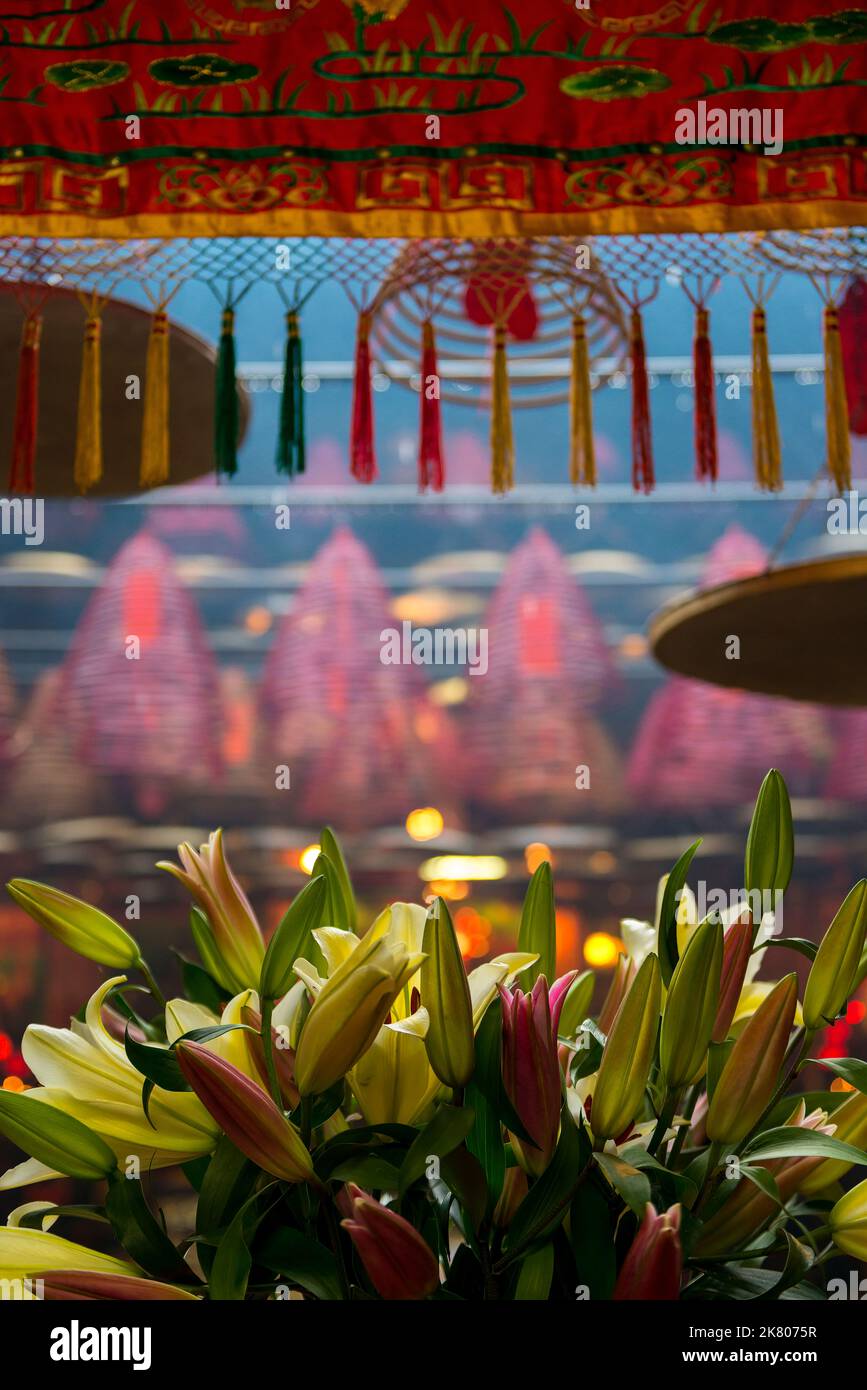 Detail of fresh lilies, embroidered decorations and spiral incense colis in the Tin Hau Temple, Yau Ma Tei, Kowloon, Hong Kong Stock Photo