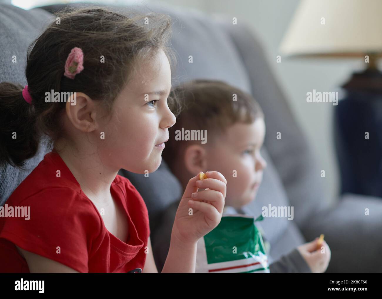 Brother and sister are eating chips and watching an amusing TV program Stock Photo