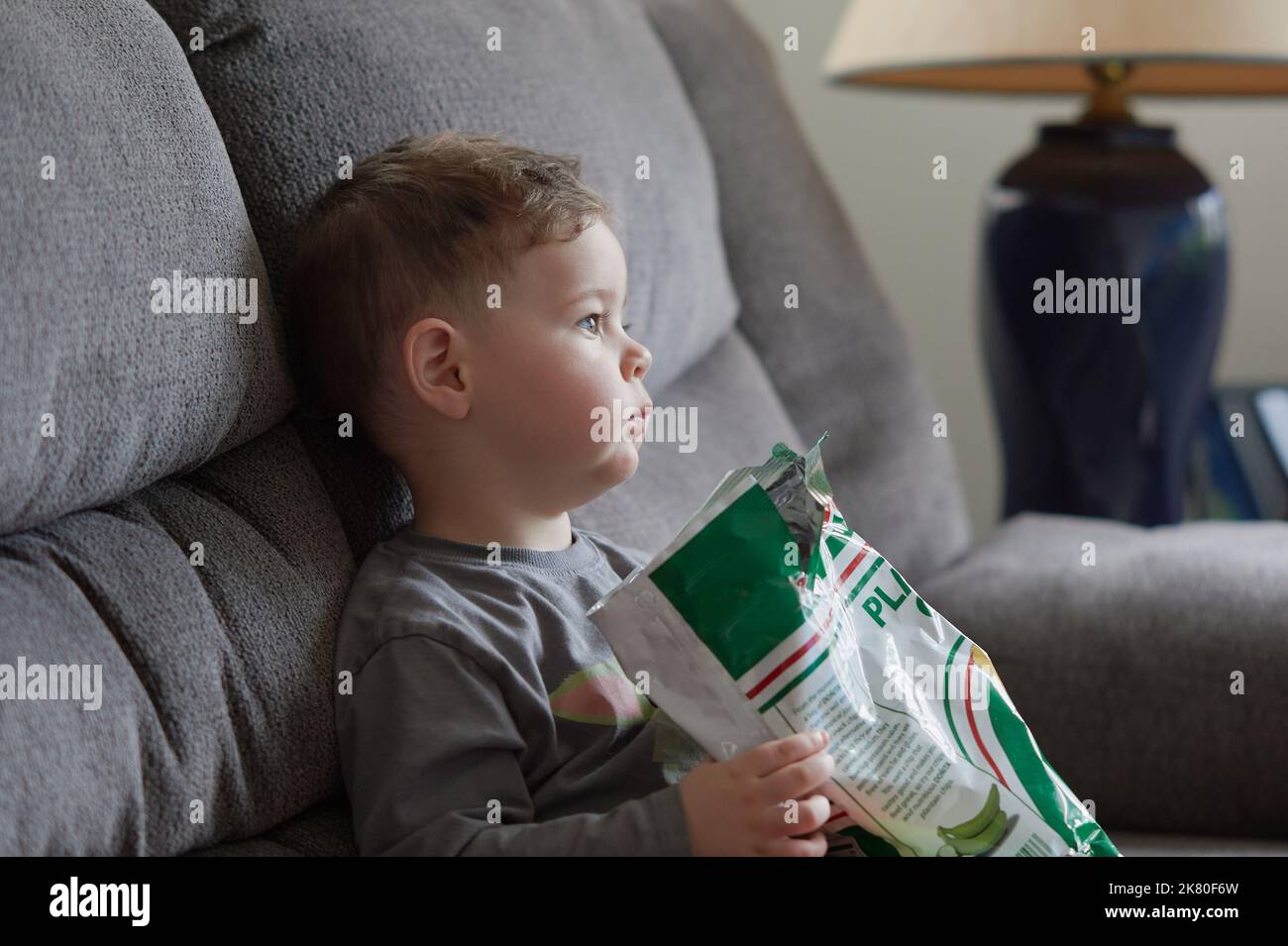 Cute boy is eating chips and watching an amusing TV program Stock Photo