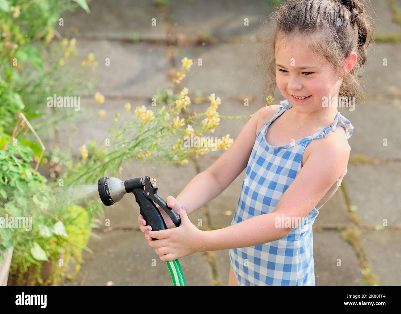 Young girl is watering plants in the backyard while wearing a bathing