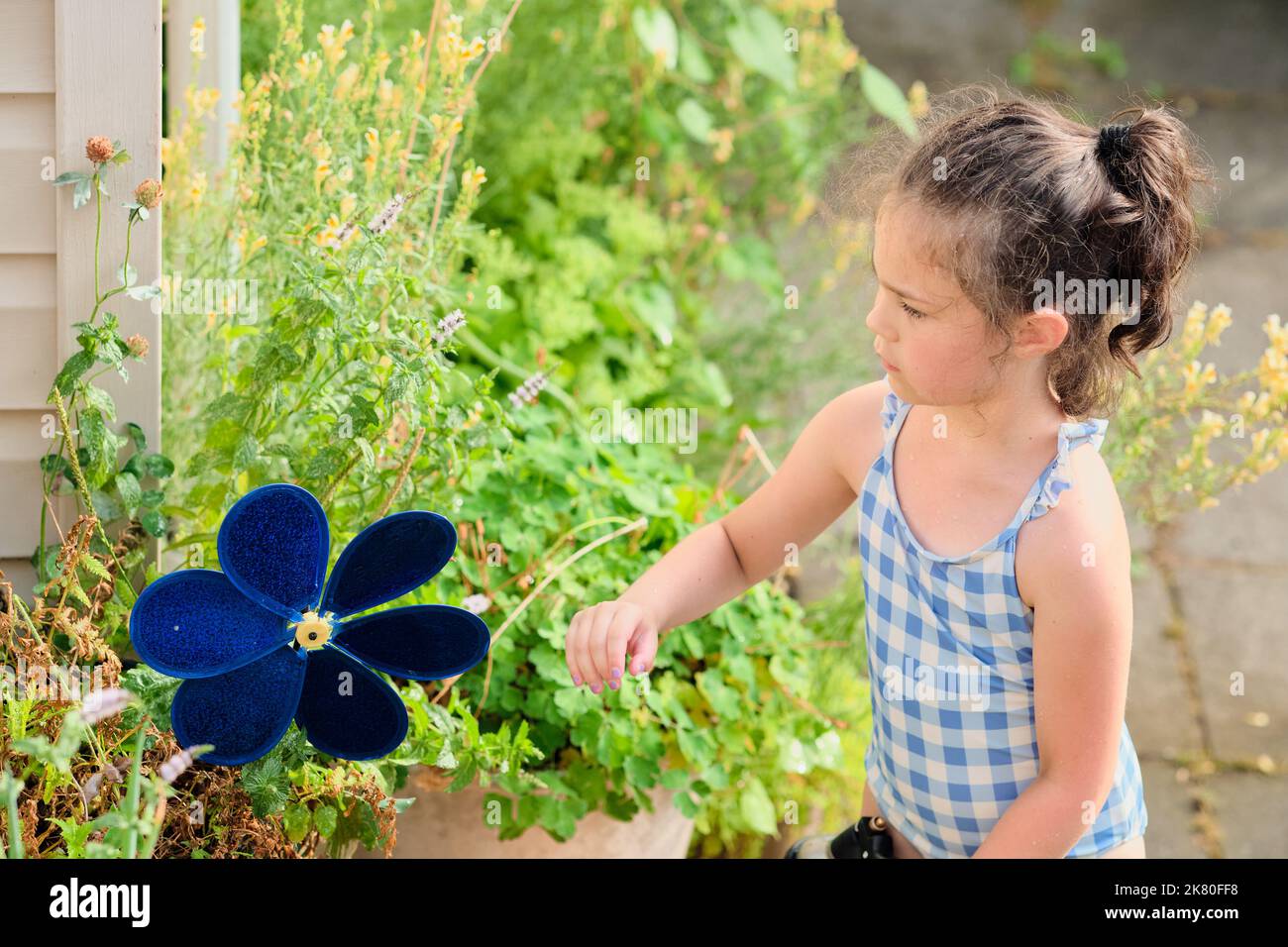 Young girl is watering plants in the backyard while wearing a bathing