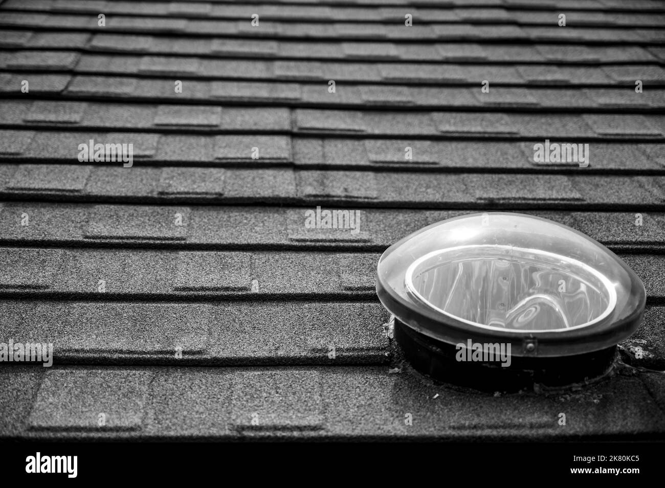 Dome shaped solar tube skylight on asphalt shingle roof  Stock Photo