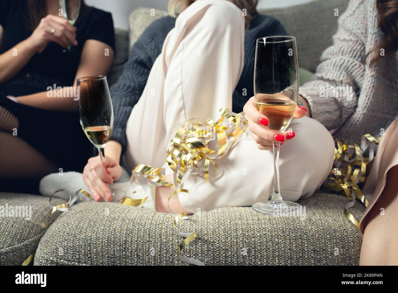 Girls sit on the couch with glasses of champagne, a house party. Front