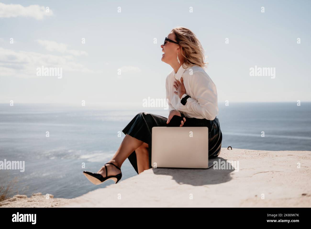 Digital nomad, Business woman working on laptop by the sea. Pretty lady typing on computer by the sea at sunset, makes a business transaction online Stock Photo