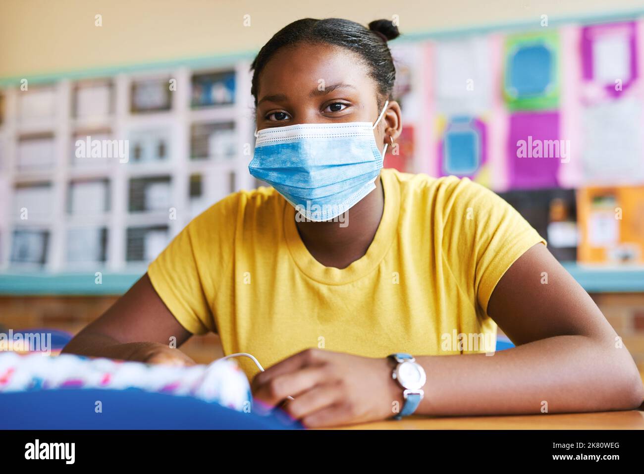 A mask at school is the new normal. a young girl sitting alone in her