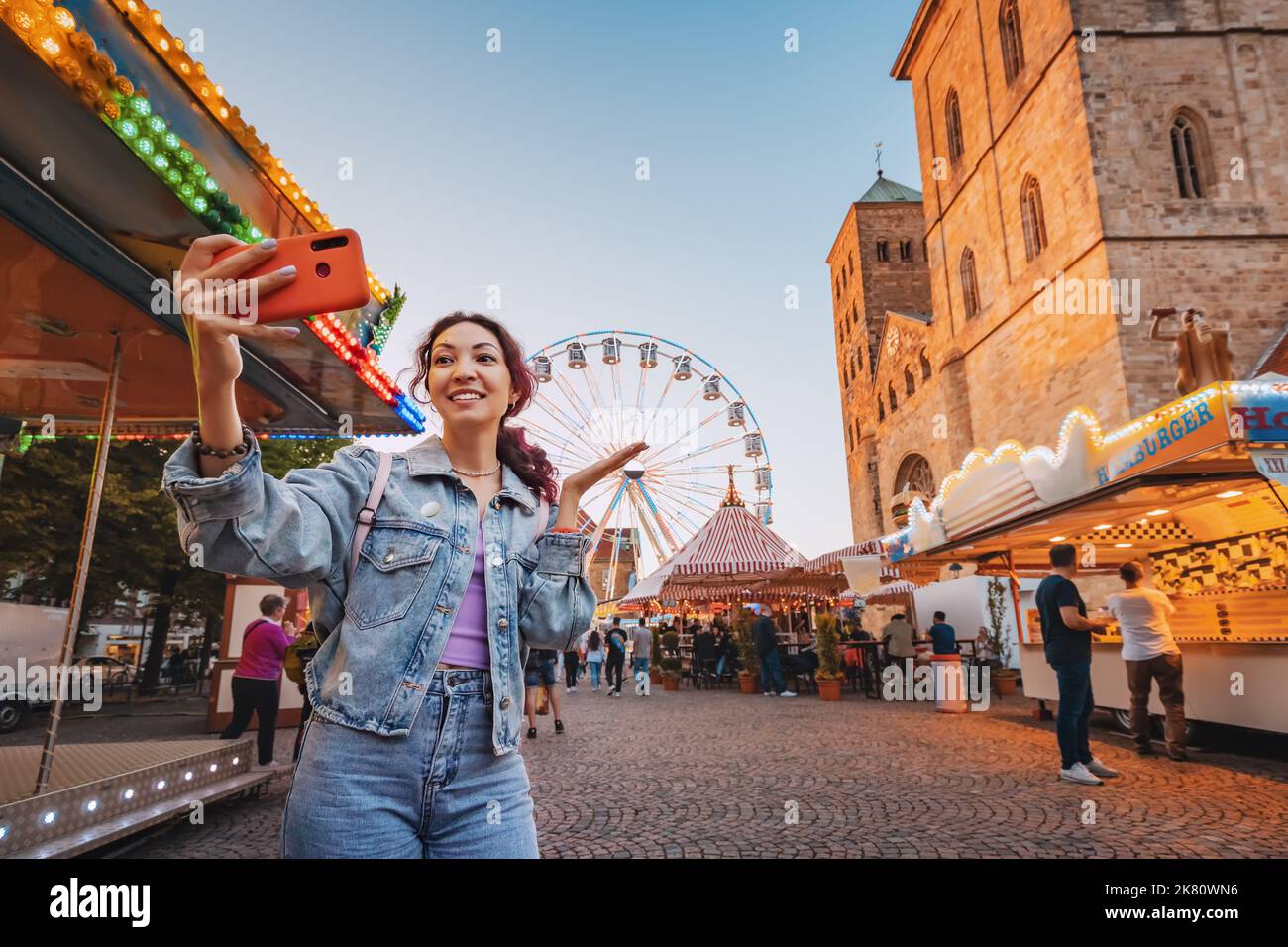 A traveler girl takes a selfie photo for social networks at an amusement fair with a Ferris wheel in the old European city on the square Stock Photo
