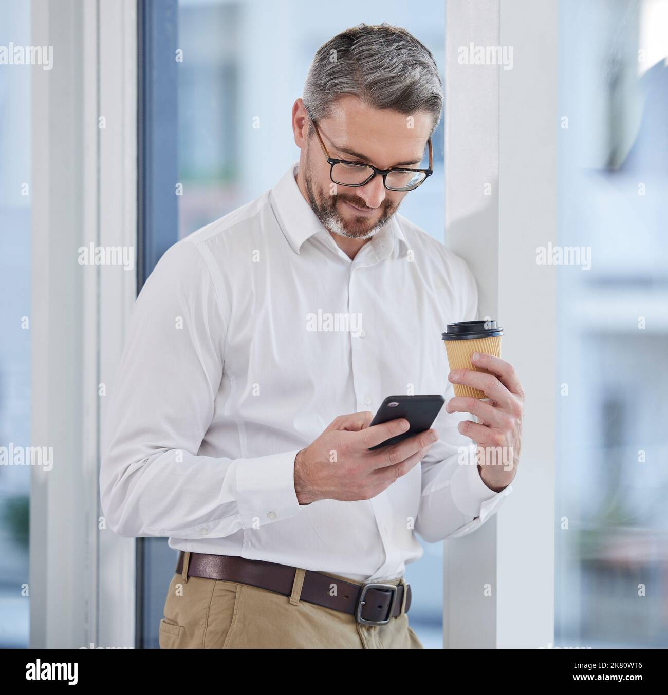 This coffee is doing wonders. a businessman using his smartphone while drinking coffee. Stock Photo