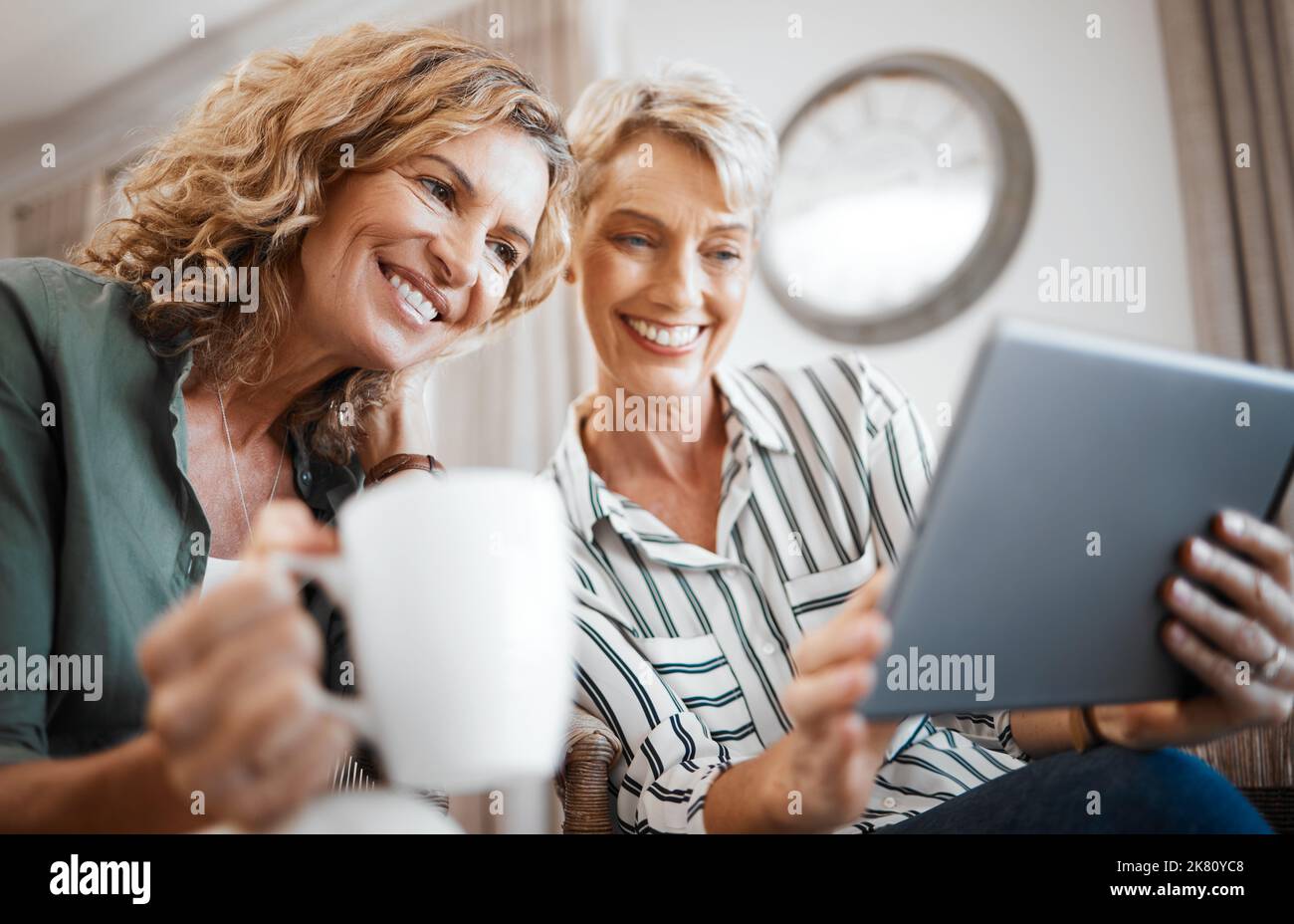 That video is hilarious. two female friends drinking coffee while using a digital tablet. Stock Photo